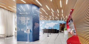 Eine moderne Lobby mit einer Rezeption, einem blauen Infostand und einer Weltkarte an der Wand.