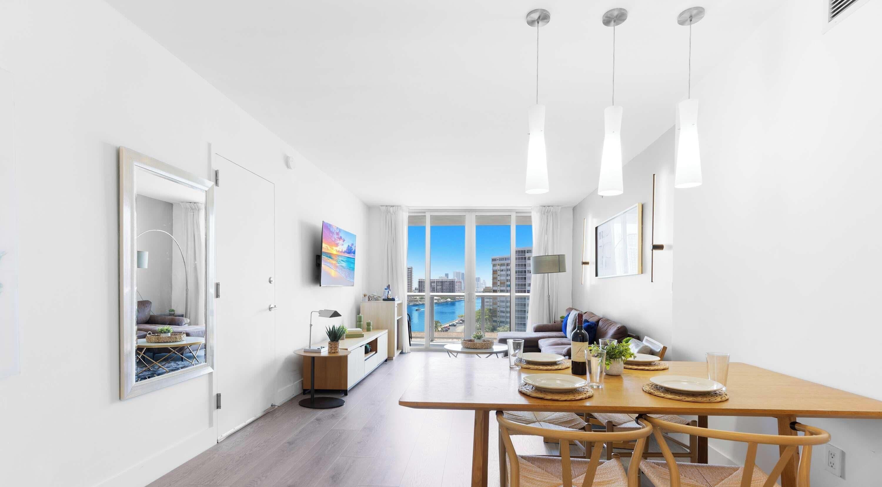 A modern hotel room with a dining area, a view of the cityscape, and a balcony.
