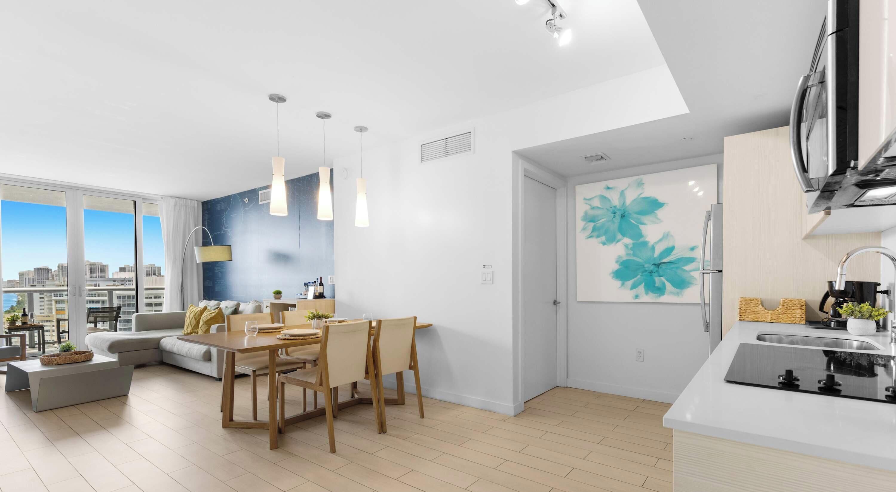 A modern apartment with a dining area, kitchen, and large windows offering a city view.