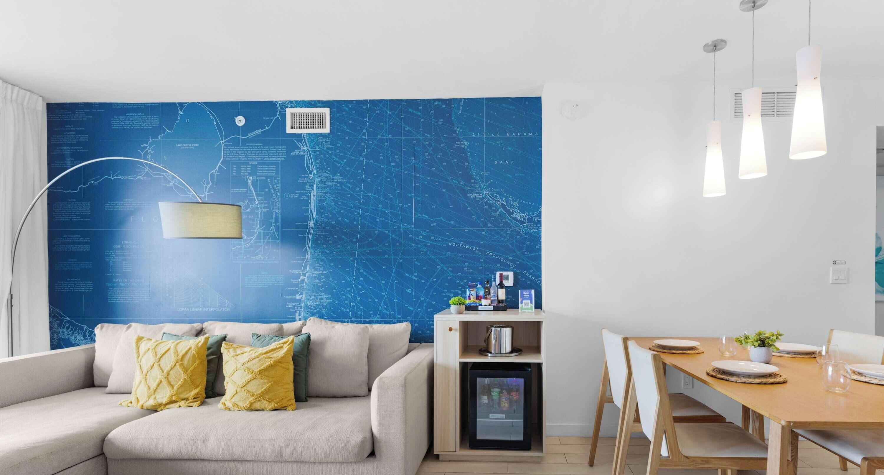 En moderne stue med en blå væg i maritim stil, en sofa med gule puder, et spiseområde med et træbord og hængende lamper.