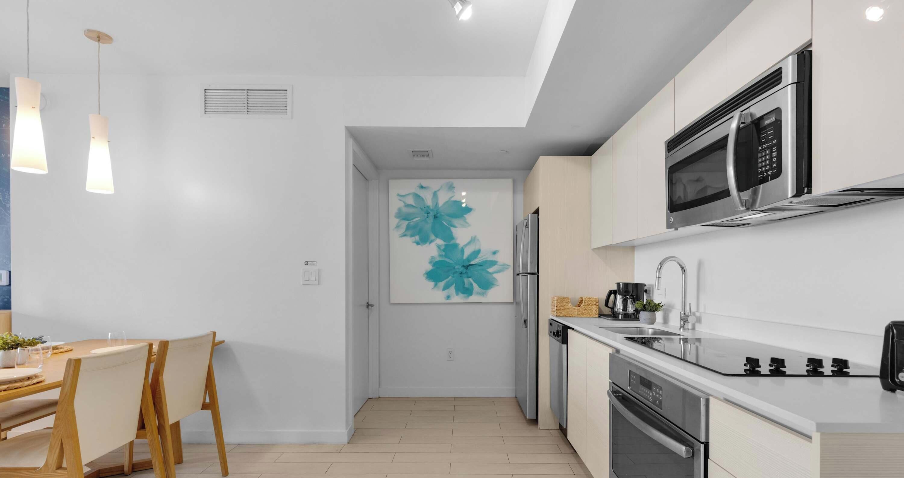 A modern kitchen with stainless steel appliances, a dining area with wooden chairs, and a wall-mounted artwork.