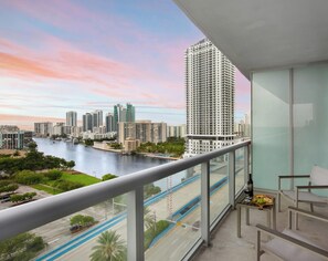 A balcony with a city view, a table with a bottle and fruit, and a chair. - New! Chic Studio with Marina & Intracoastal View (Hallandale Beach)