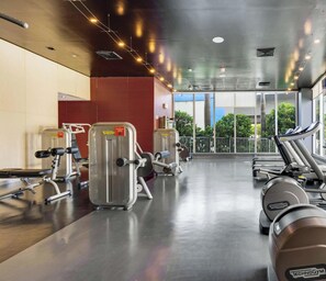 Ein Fitnessraum mit Cardiogeräten, Gewichten und großen Fenstern mit Blick ins Freie.