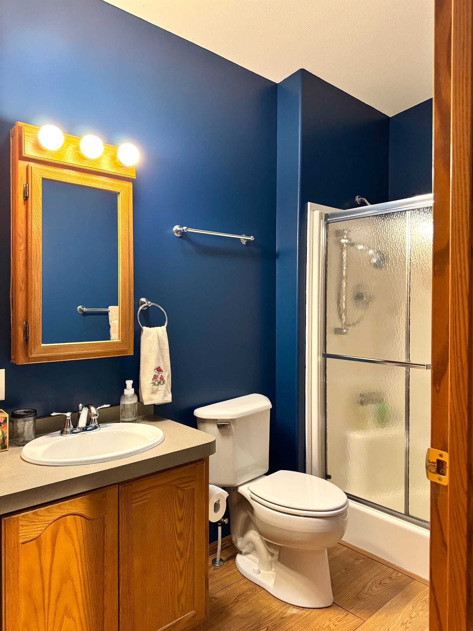 Een badkamer met een houten wastafelmeubel, een wit toilet, een douchecabine van glas en een spiegel met verlichting.