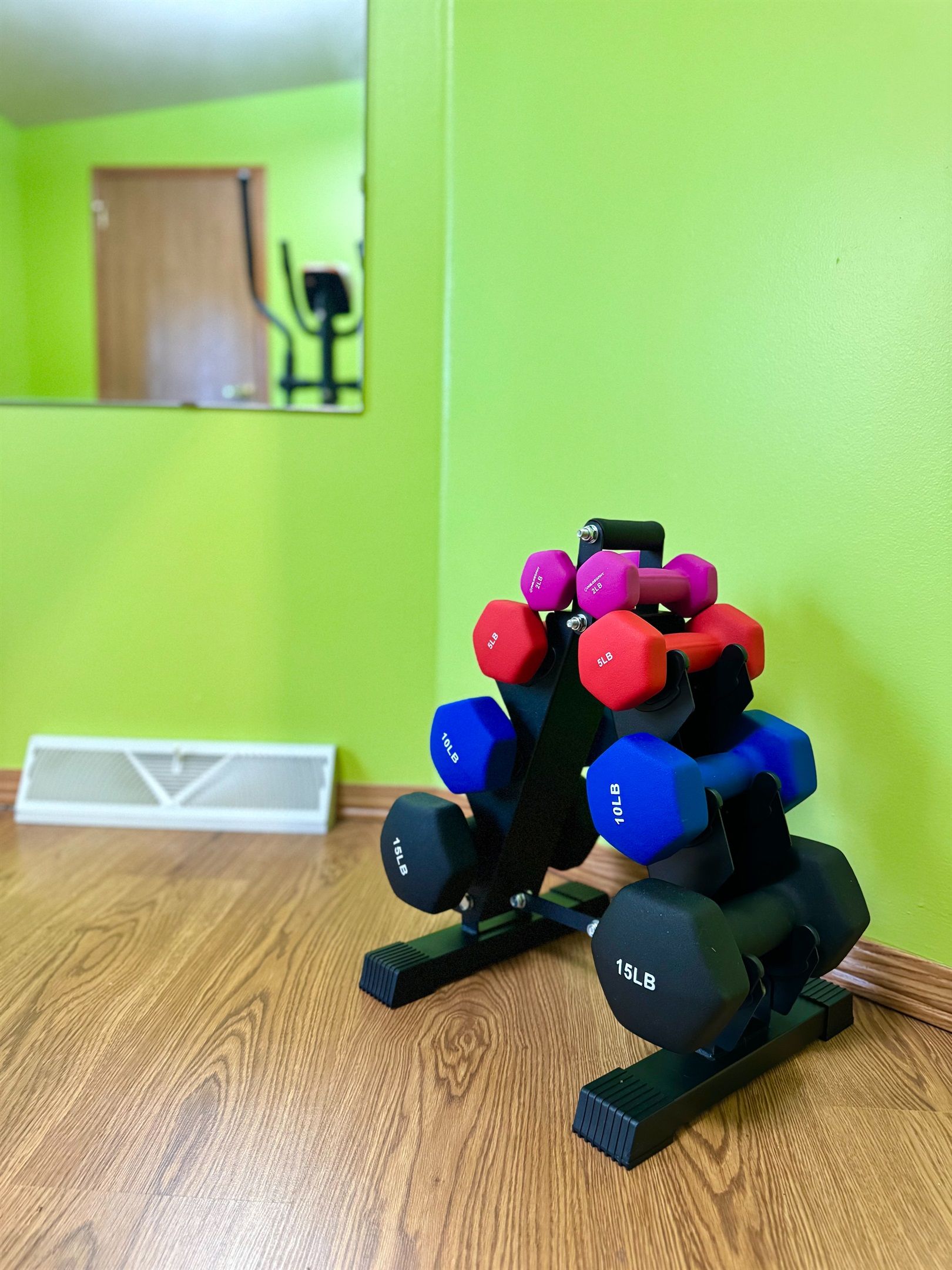 A set of dumbbells on a wooden floor with a green wall and a door in the background.