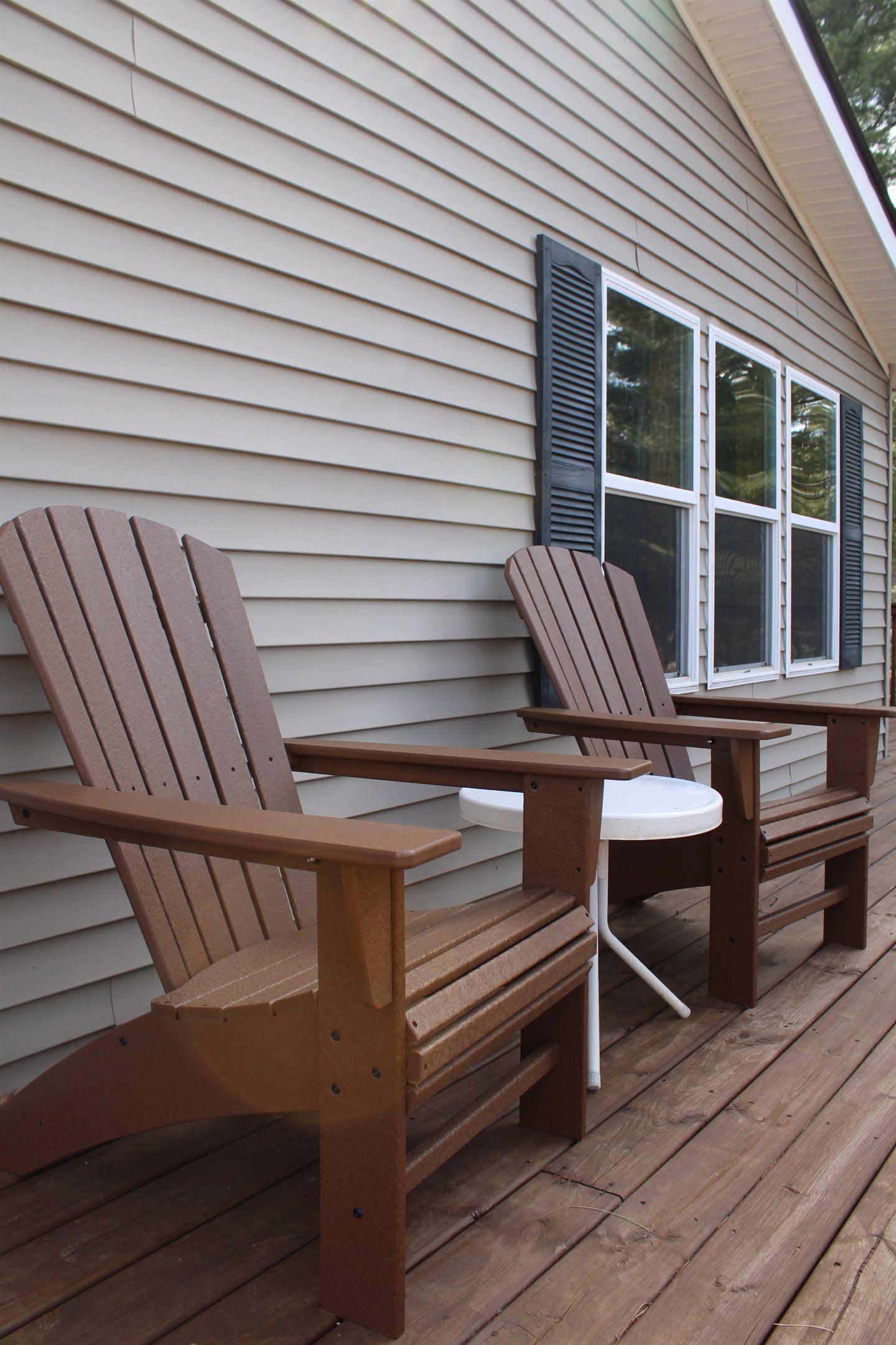 Una terraza de madera con dos sillas Adirondack y una mesita.