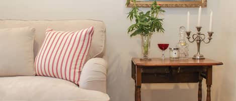 Un sofá color beige con un cojín a rayas, una mesita de madera con un jarrón, velas y un decantador de vidrio.