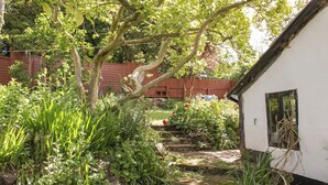A garden with a white building, a wooden fence, and a stone pathway. - Upper Frogpool Cottage (Crediton)