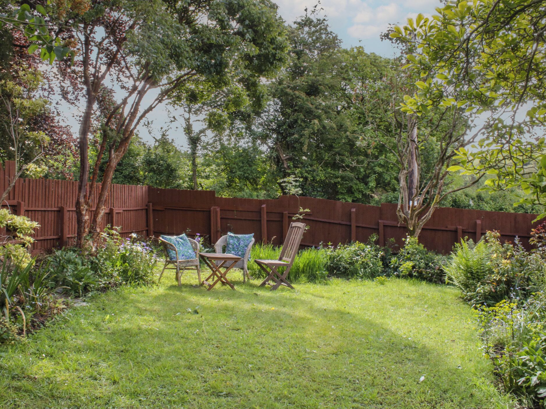 A backyard with a wooden fence, a grassy lawn, and two chairs.