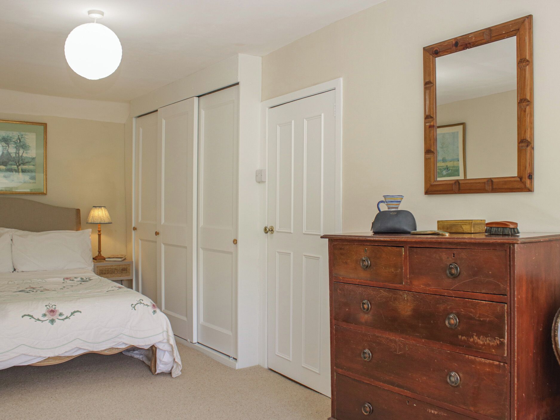 A bedroom with a bed, dresser, mirror, and a door leading to another room.