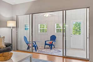 Ein Zimmer mit einer Schiebetür zu einer Terrasse, auf der zwei blaue Stühle und ein kleiner Tisch stehen.