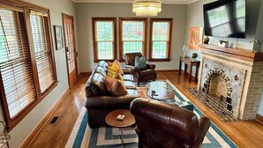 A living room with a sofa, armchairs, a coffee table, a fireplace, and a TV mounted on the wall. - Hill Street Retreat (Oklahoma City)