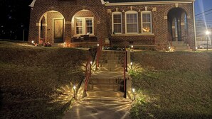 A brick house with a front porch, a staircase, and a well-lit entrance. - Hill Street Retreat (Oklahoma City)