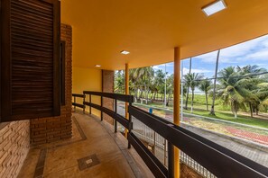 A balcony with a brick wall, a railing, and a view of palm trees and a road.