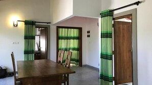 Un comedor con una mesa y sillas de madera, un ventilador de techo y una puerta con cortina verde y blanca a rayas.