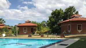 Una piscina con un borde de baldosas, rodeada de edificios de ladrillo con techos de tejas rojas y palmeras al fondo.