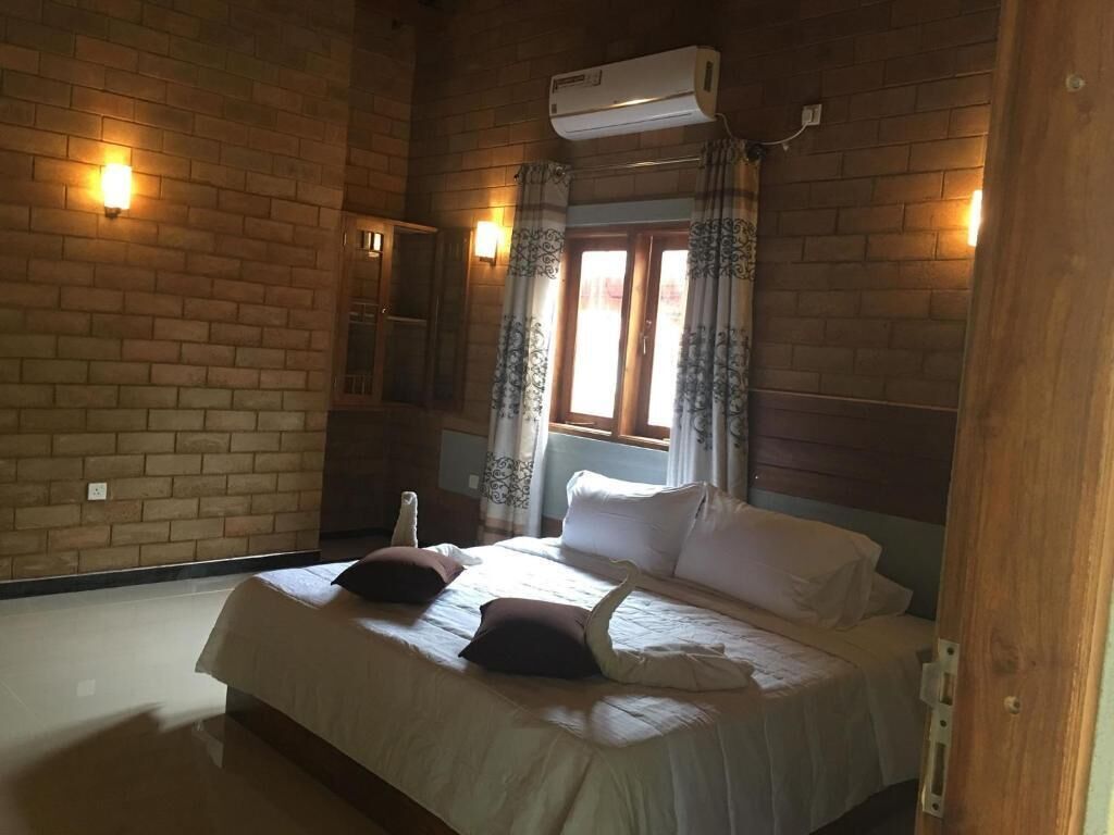 Une pièce avec un mur en briques, un lit avec une literie blanche, une fenêtre avec des rideaux et un appareil de climatisation.