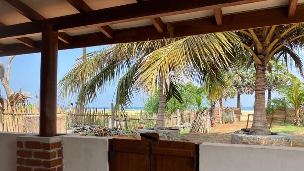 Un espacio al aire libre cubierto con una mesa de madera, un muro de ladrillo y vistas a la playa con palmeras.
