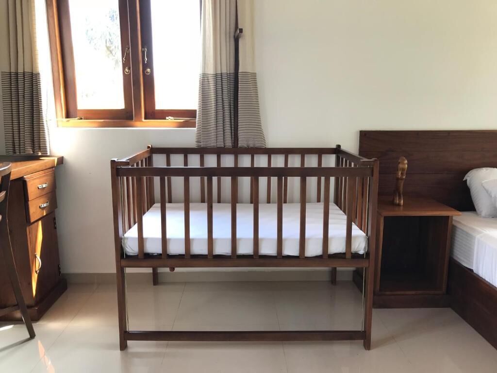 Una cuna de madera en una habitación con ventana, cómoda y cama.