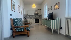 A modern kitchen with white cabinets, a dining area with a wooden table and chairs, a sofa with patterned cushions, and a television on a stand. - "Window to the Sea" Spacious and new sea view apartment (Marina di San Vito)