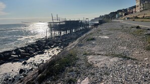 A coastal walkway with a rocky shore, a pier extending into the sea, and buildings in the background. - "Window to the Sea" Spacious and new sea view apartment (Marina di San Vito)