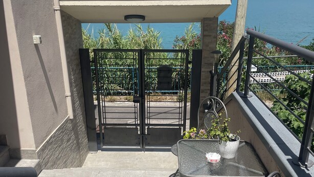 A balcony with a table and chairs, a view of the sea, and a gate leading to a garden. - "Window to the Sea" Spacious and new sea view apartment (Marina di San Vito)