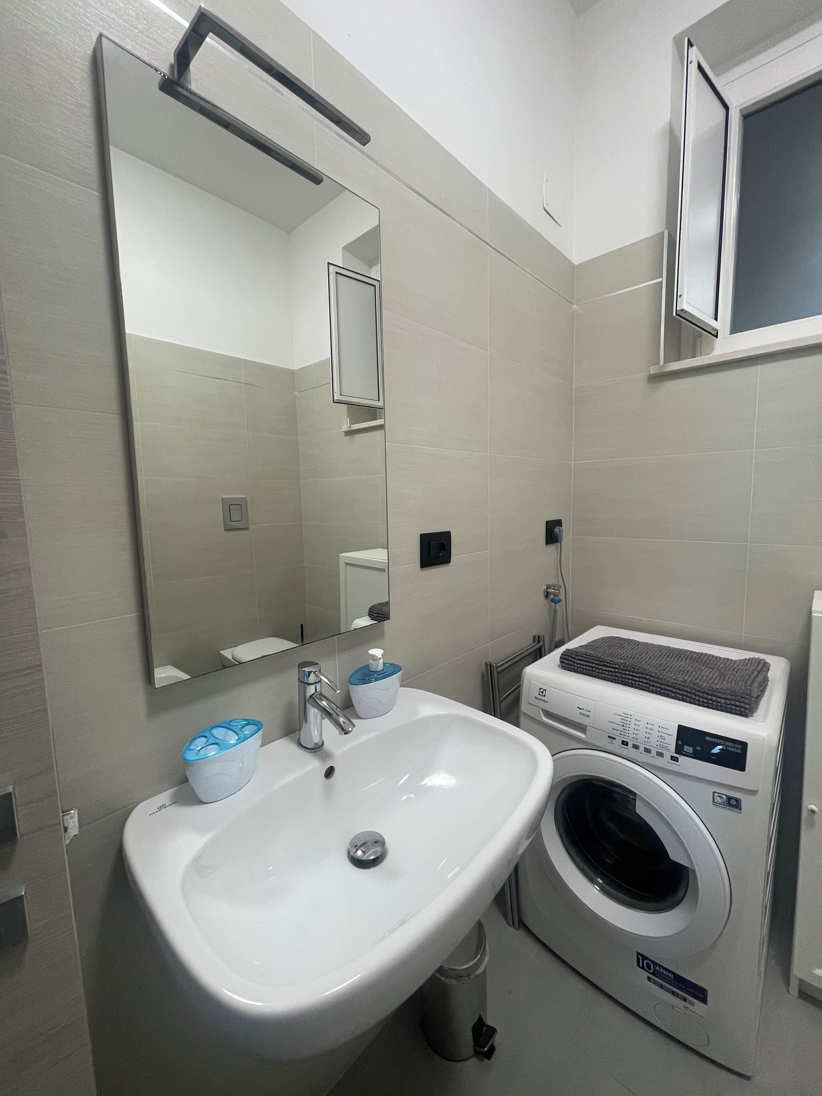 Baño con lavamanos, espejo, toallero y lavadora.