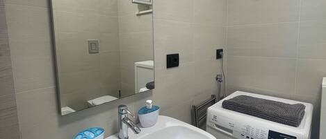 Baño con lavamanos, espejo, toallero y lavadora.