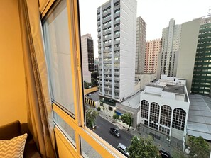 A view from a window overlooking a cityscape with tall buildings, a street with cars, and a building with large windows. - LK Centro 10 (Belo Horizonte)