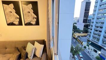 Quarto com sofá, duas pinturas emolduradas de animais e vista para uma rua da cidade.