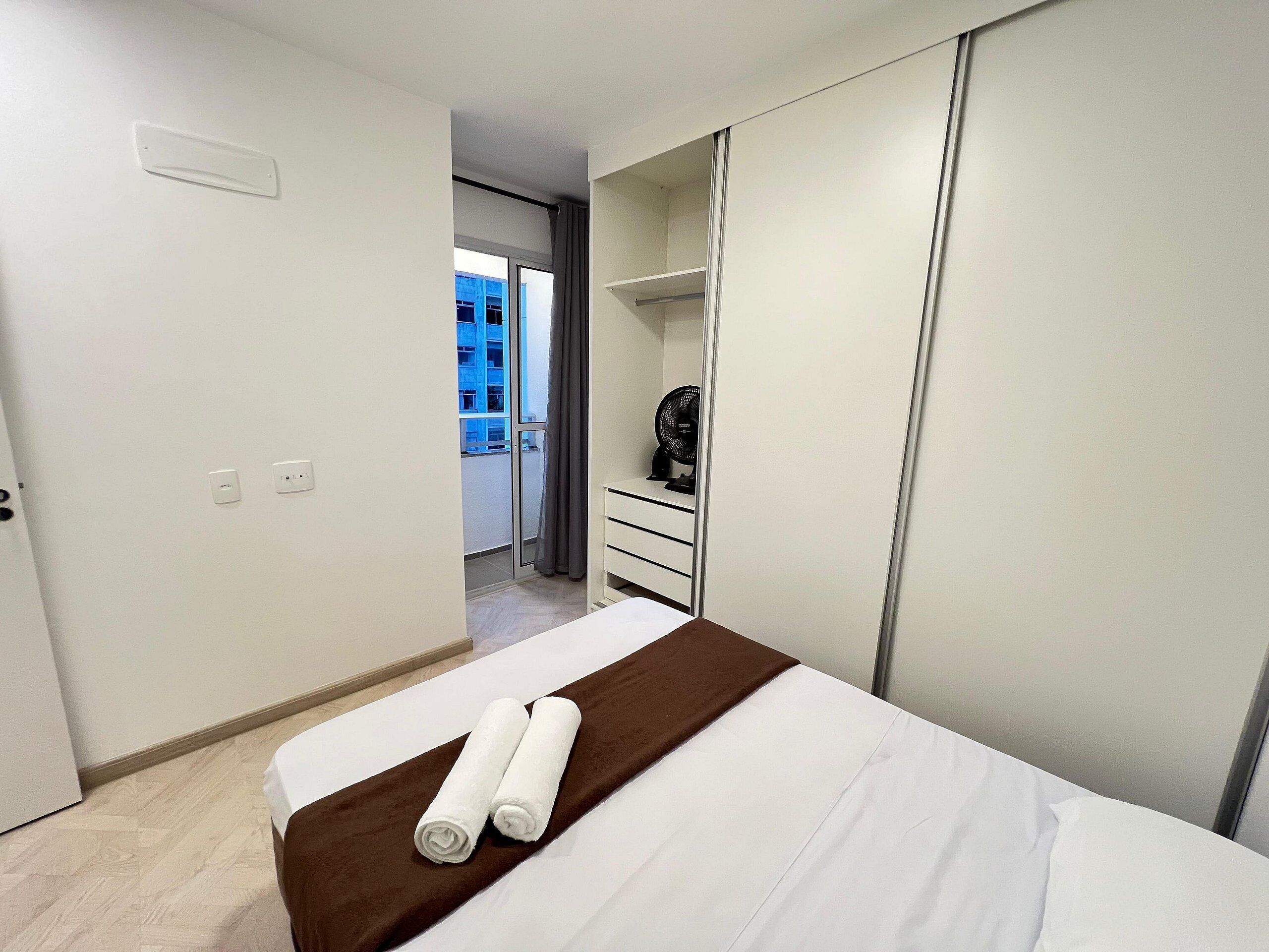 Un dormitorio con cama, cómoda, ventilador y vista a un edificio.