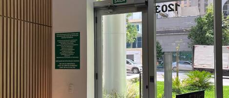 Un área de recepción con un banco de madera, una puerta de vidrio con un letrero que dice 'SAÍDA' y vista a la calle.