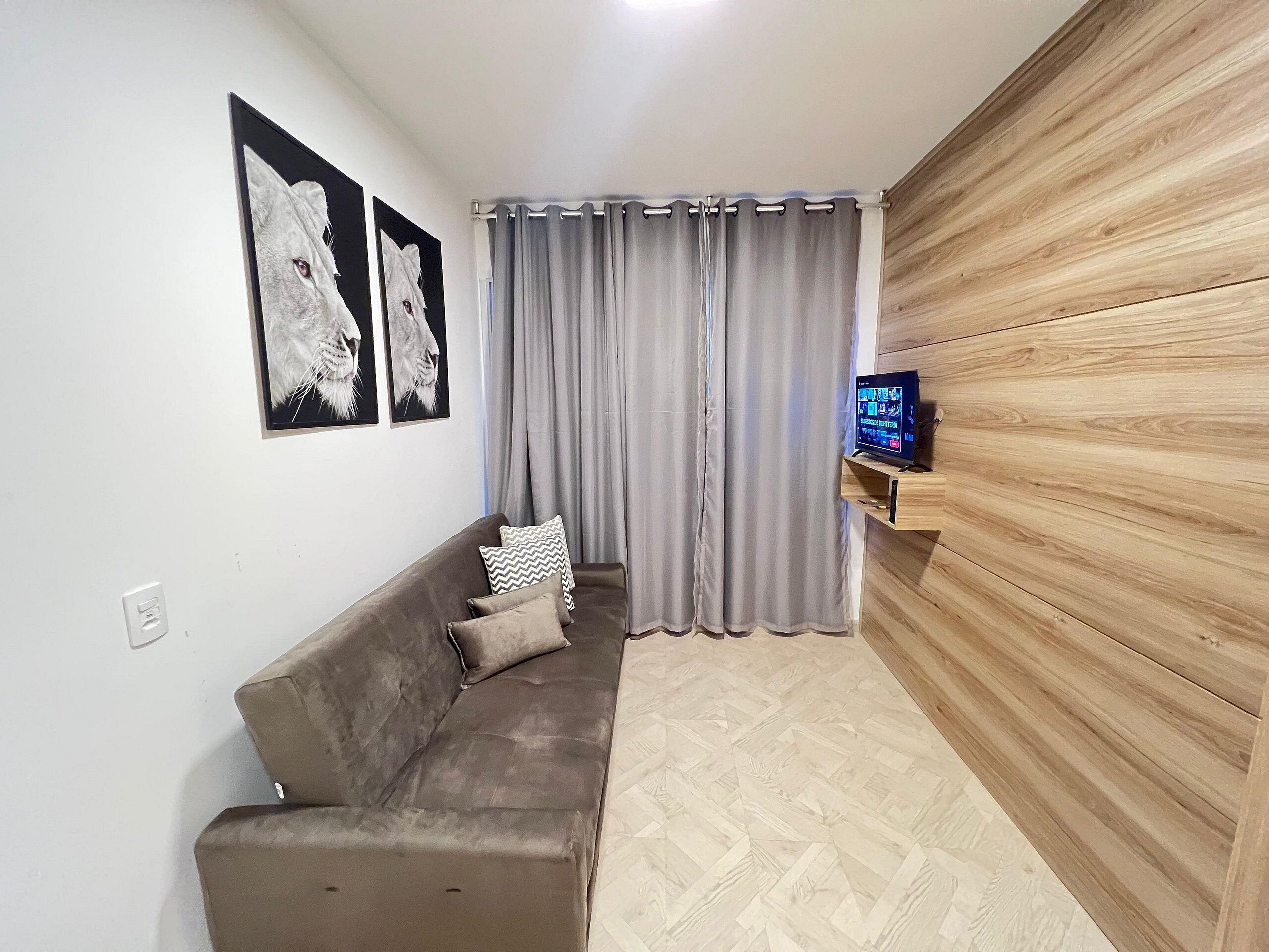 A living room with a sofa, a TV on a wooden stand, grey curtains, and wall art.