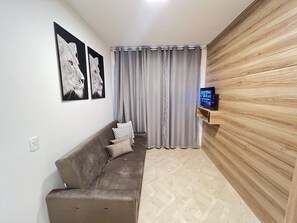 A living room with a sofa, a TV on a wooden stand, grey curtains, and wall art. - LK Centro 10 (Belo Horizonte)