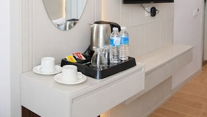 Ett modernt hotellrum med en platt-TV som är monterad på väggen, en kaffestation med koppar och en vattenkokare samt en stor spegel ovanför disken.