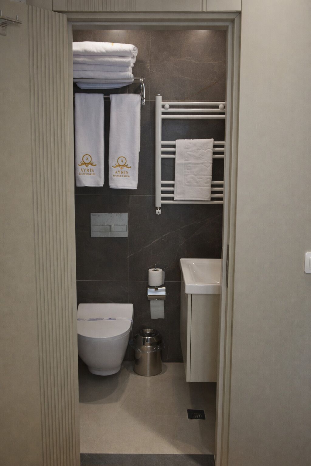 A compact bathroom with a toilet, sink, towel rack, and a trash bin.