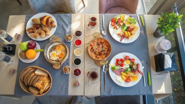 Ett bord dukat med olika rätter, inklusive croissanter, frukt och en sallad, samt tillbehör och drycker.