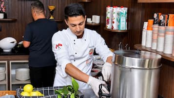 Un chef preparando comida en una cocina con una olla de acero inoxidable grande, un tazón de limones y una cesta de hojas verdes.