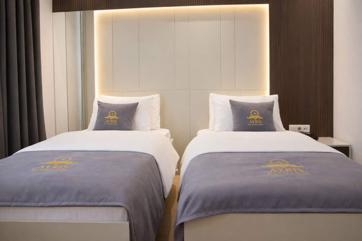 Habitación de hotel con dos camas, cada una con cubrecama y almohadas que muestran el logotipo del hotel.