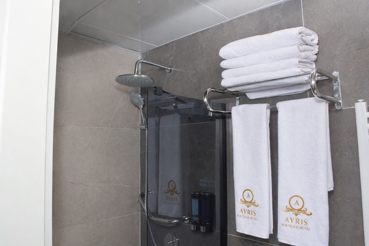 A modern bathroom with a glass-enclosed shower, a towel rack with folded towels, and a visible bottle of shampoo.