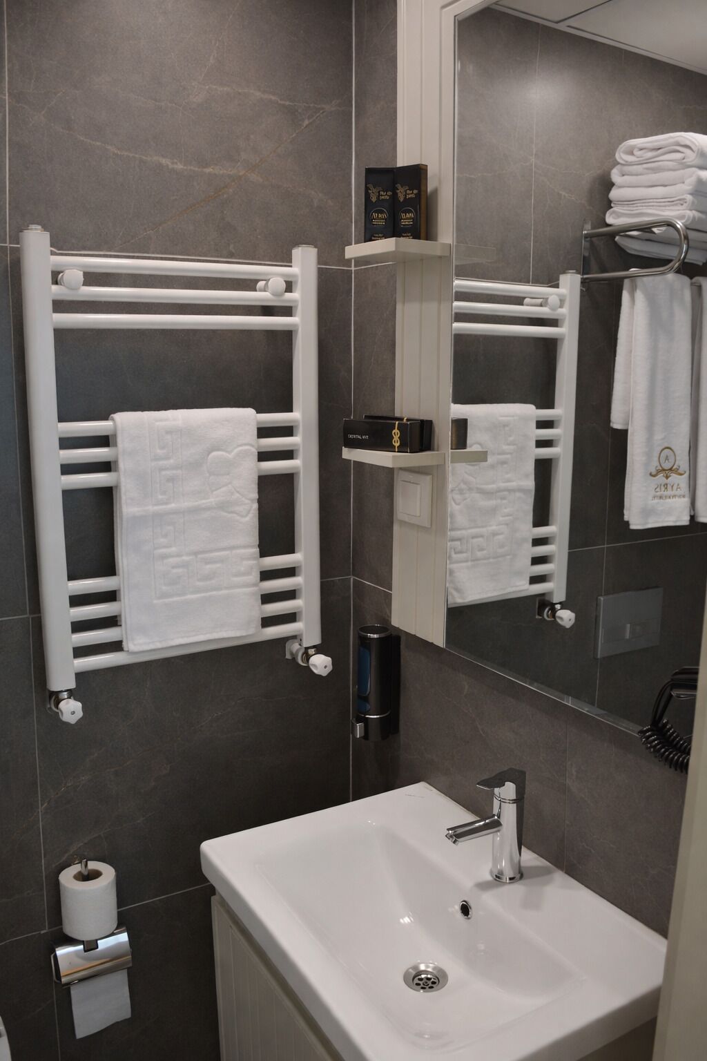 Un baño moderno con un lavamanos blanco, toalleros y un espejo.