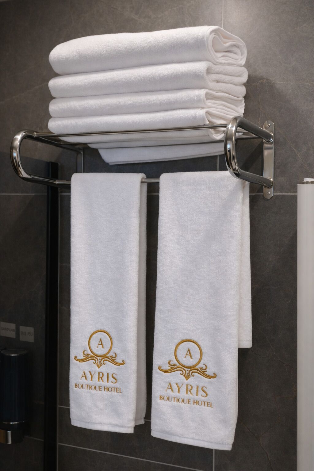 Ein Badezimmer mit einem Handtuchhalter, der gefaltete Handtücher und zwei Handtücher mit eingestickten Logos trägt.