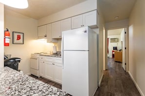 A compact kitchen with white cabinets, a refrigerator, a stove, and a microwave. - Maple Row Apartment: Perfect for Game Day! (Bloomington)