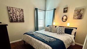 Een slaapkamer met een bed, een plafondventilator, een raam met gordijnen en kunst aan de wanden.
