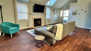 Een ruime woonkamer met een hoge plafond, een open haard, een televisie en een groot raam.