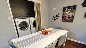 Een eethoek met een tafel, stoelen, een wasmachine en een decoratief wandobject.
