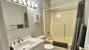Een badkamer met een wastafel, wastafelmeubel, spiegel en douche.