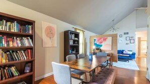 A spacious living room with a wooden dining table, a bookshelf, and a blue sofa. - Blush Bungalow: Cozy Home Near Downtown Bloomington (Bloomington)