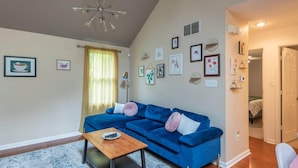 A living room with a blue sofa, a wooden coffee table, and a chandelier. - Blush Bungalow: Cozy Home Near Downtown Bloomington (Bloomington)