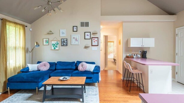 A living room with a blue sofa, a wooden coffee table, and a kitchen area with a pink countertop and bar stools. - Blush Bungalow: Cozy Home Near Downtown Bloomington (Bloomington)